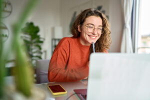 Happy young woman using laptop sitting at desk while working from home